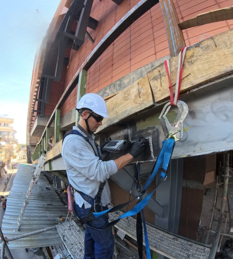 Técnico con arnés inspeccionando con equipo de ultrasonido una estructura metálica de fachada