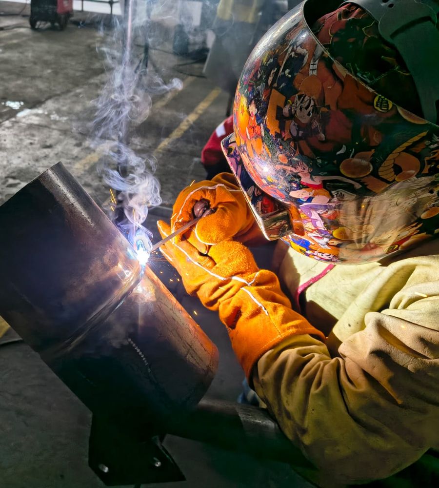 Soldador ejecutando soldadura en una junta de tubería en taller